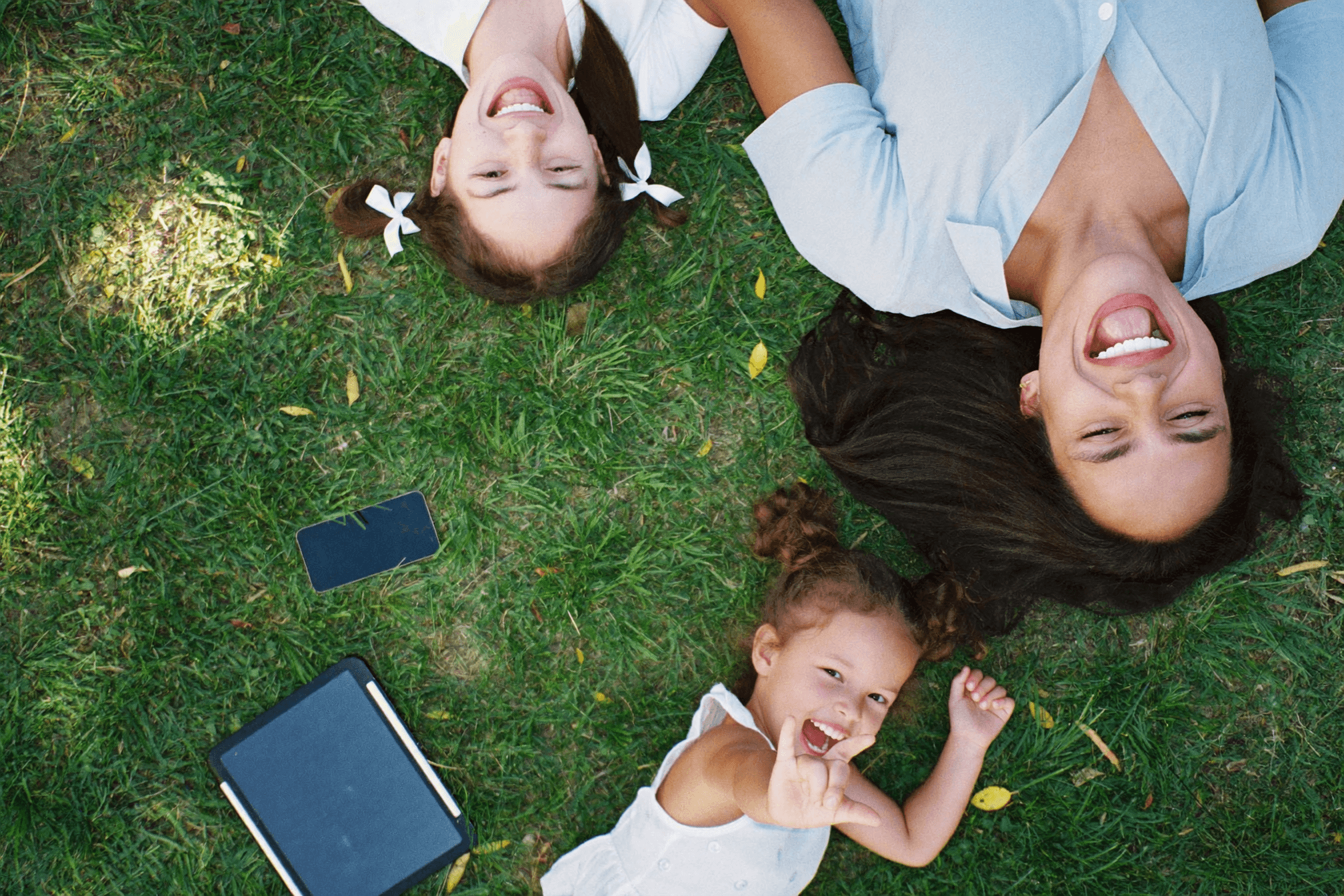A family laughing together on the grass, their phone left face down beside them